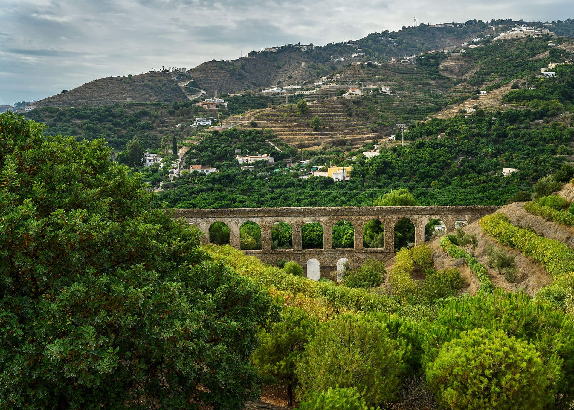 The old aqueduct crossing a green, terraced valley below the hill.