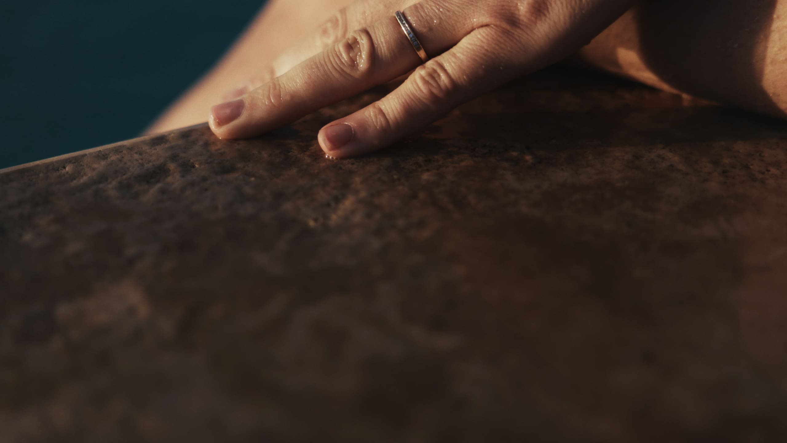 A hand resting on sun-warmed stone at the pool's edge.