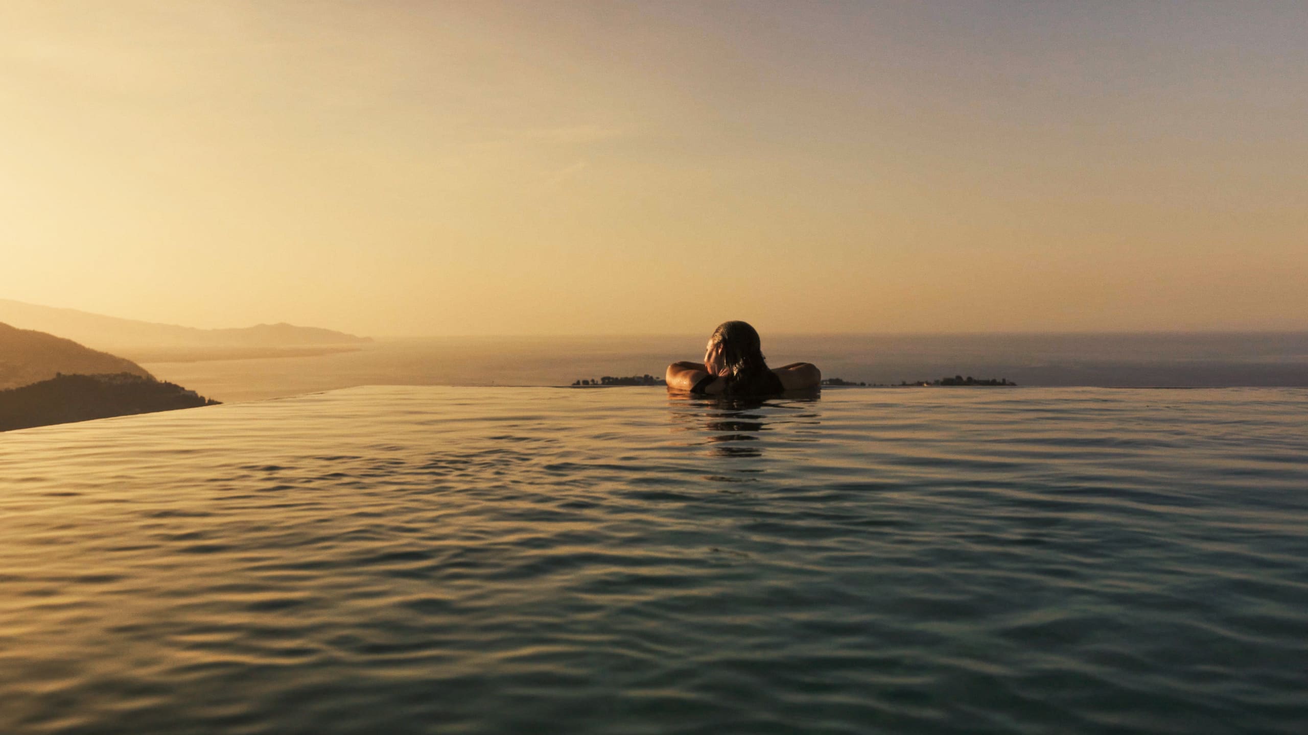 A guest resting at the edge of the infinity pool, the coast fading into the sunset.
